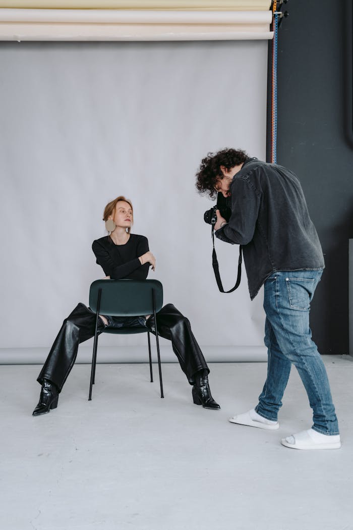 Photographer capturing a model sitting on a chair during a studio photoshoot session.